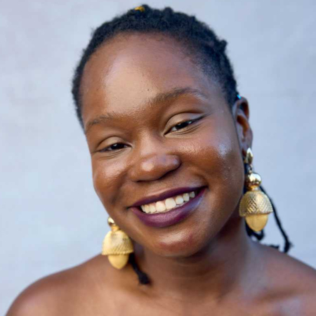 Faridah Gbadamosi in portrait. A person with dark brown eyes wears wine-red lipstick and large gold earrings.